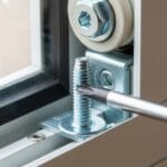 Close-up view of screwdriver removing roller mounting screw on explain How to Repair Sliding Glass Door Rollers