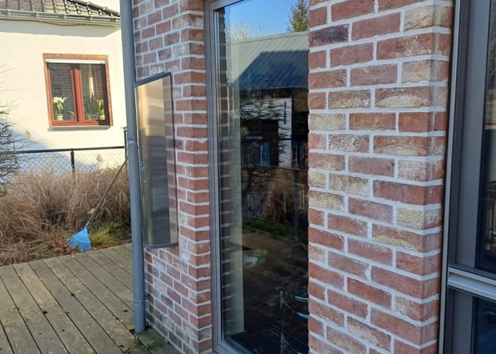 View from inside a building looking out at a small, walled courtyard where tall grass grows freely around a modern, round plant pot, with the visible window and door potentially requiring windows and door repair in Austin